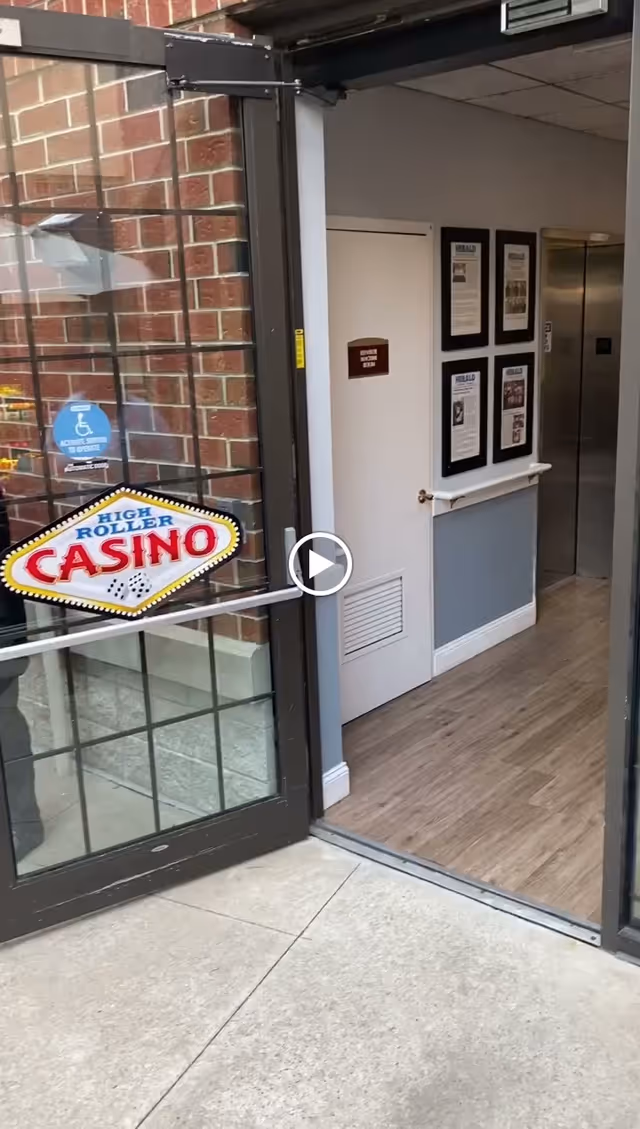 Glass entry door with a 'High Roller Casino' sticker opens into a hallway with framed notices and an elevator.