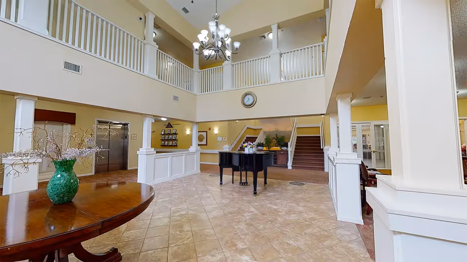 Two-story lobby/atrium with a chandelier, grand piano, reception desk, staircase and balcony railing.