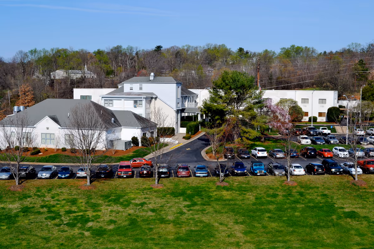 Aerial view of a senior therapy facility with white buildings, a parking lot full of cars, and a grassy lawn in front.