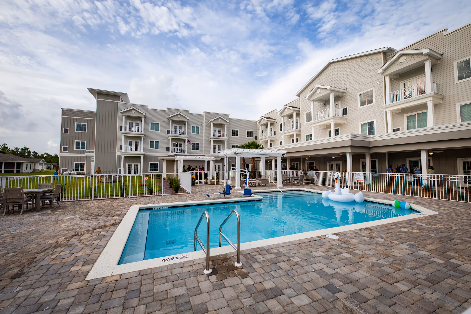 Outdoor swimming pool and paved patio in front of a multi-story senior living building with balconies.
