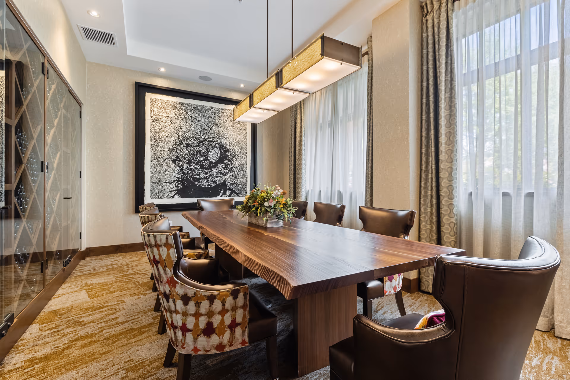 Elegant dining room with a long wooden table, upholstered chairs, a pendant light, and large windows with curtains.