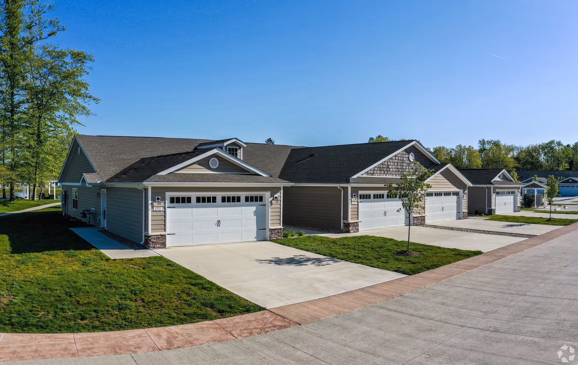 Single-story attached residential units with white garage doors, driveways, and small lawns under a clear blue sky.
