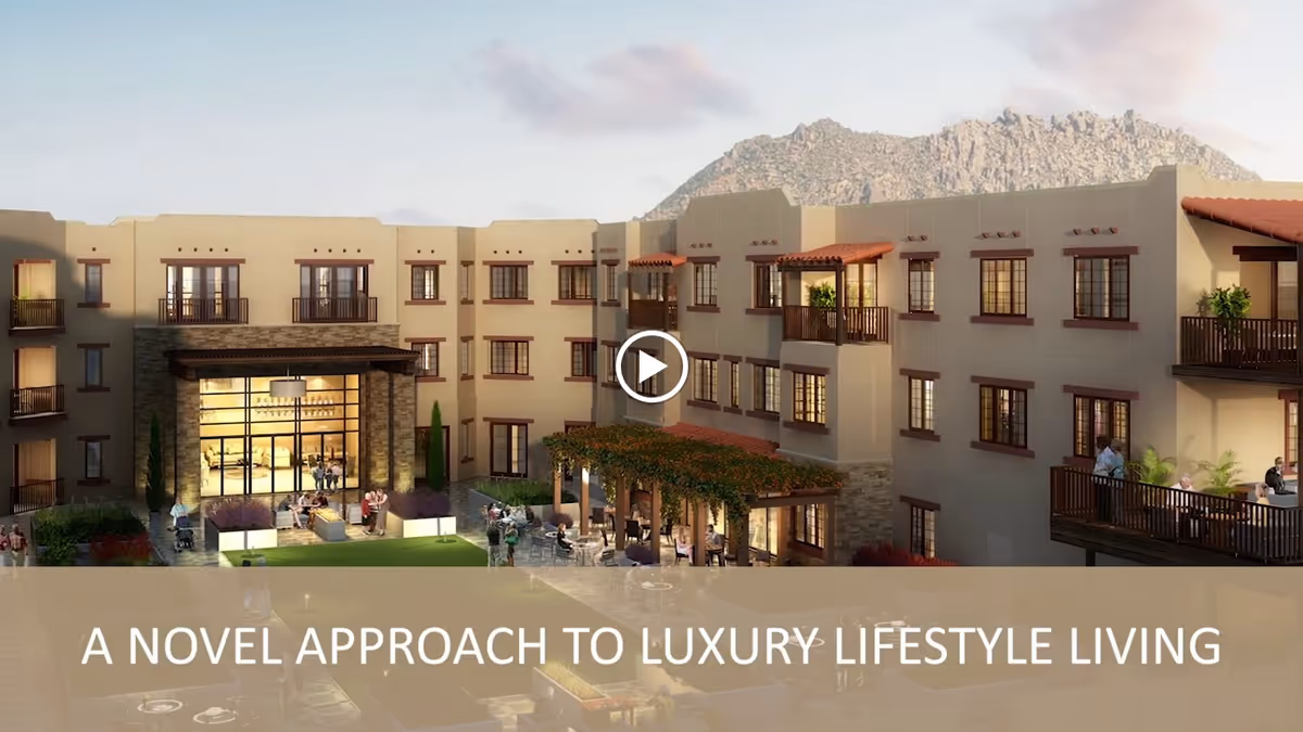Exterior view of a luxury senior living facility with a courtyard featuring outdoor seating and greenery, surrounded by a multi-story building with balconies and large windows, set against a mountainous backdrop during daylight.