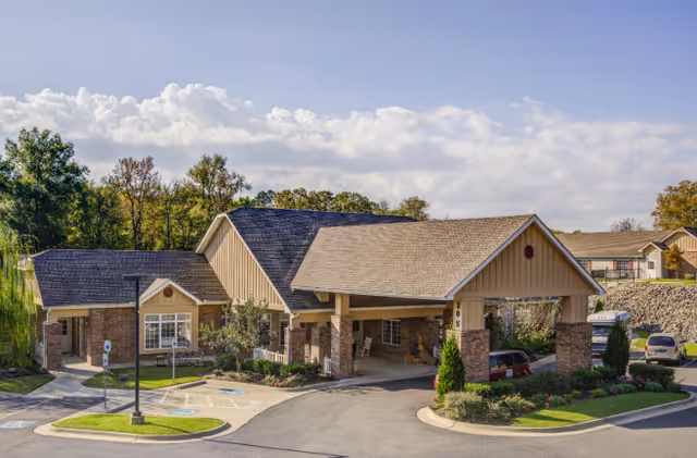 Front exterior of a single-story assisted living facility with a covered entrance, landscaped grounds, and parked cars.