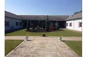 U-shaped single-story care facility surrounding a grassy courtyard with a central walkway, planters, and clear sky.