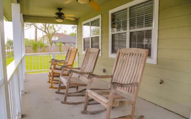 Covered porch with wooden rocking chairs along a green exterior wall overlooking a grassy yard.