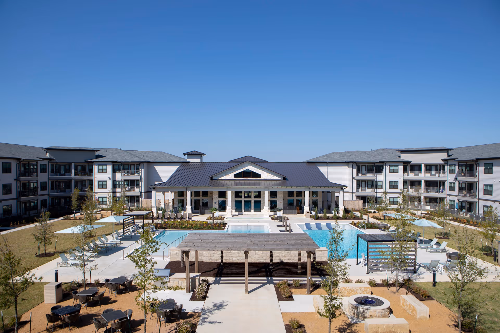 Outdoor courtyard of the Solea Keller complex with a central swimming pool, pergola, seating areas and surrounding three-story buildings under a clear blue sky.