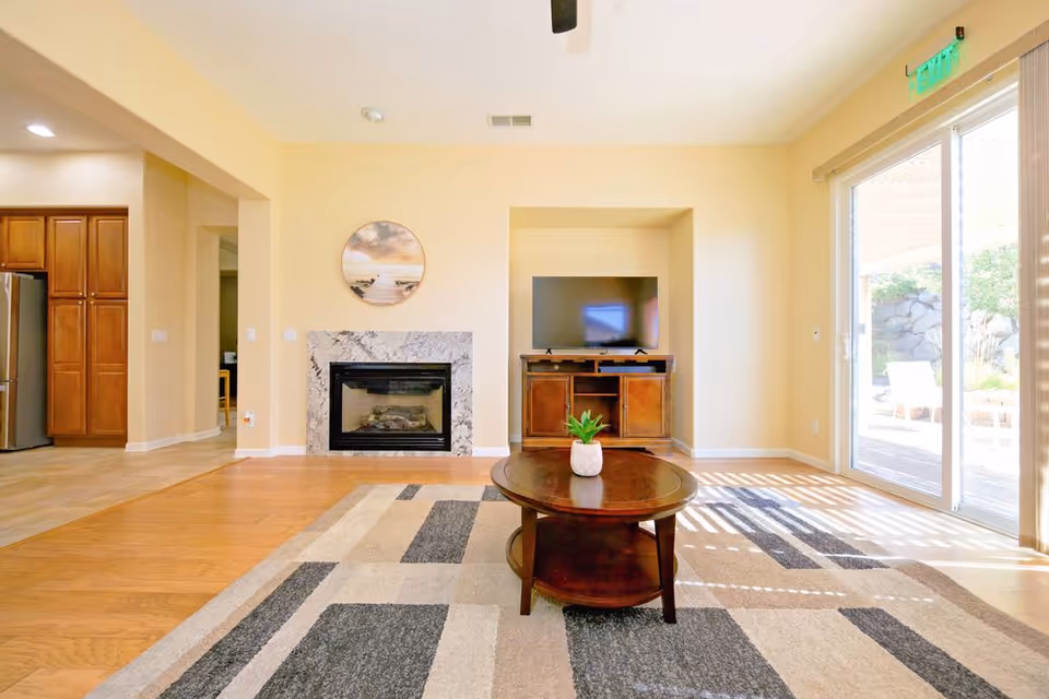 Bright living room with a fireplace, TV stand, round coffee table, and sliding glass doors.