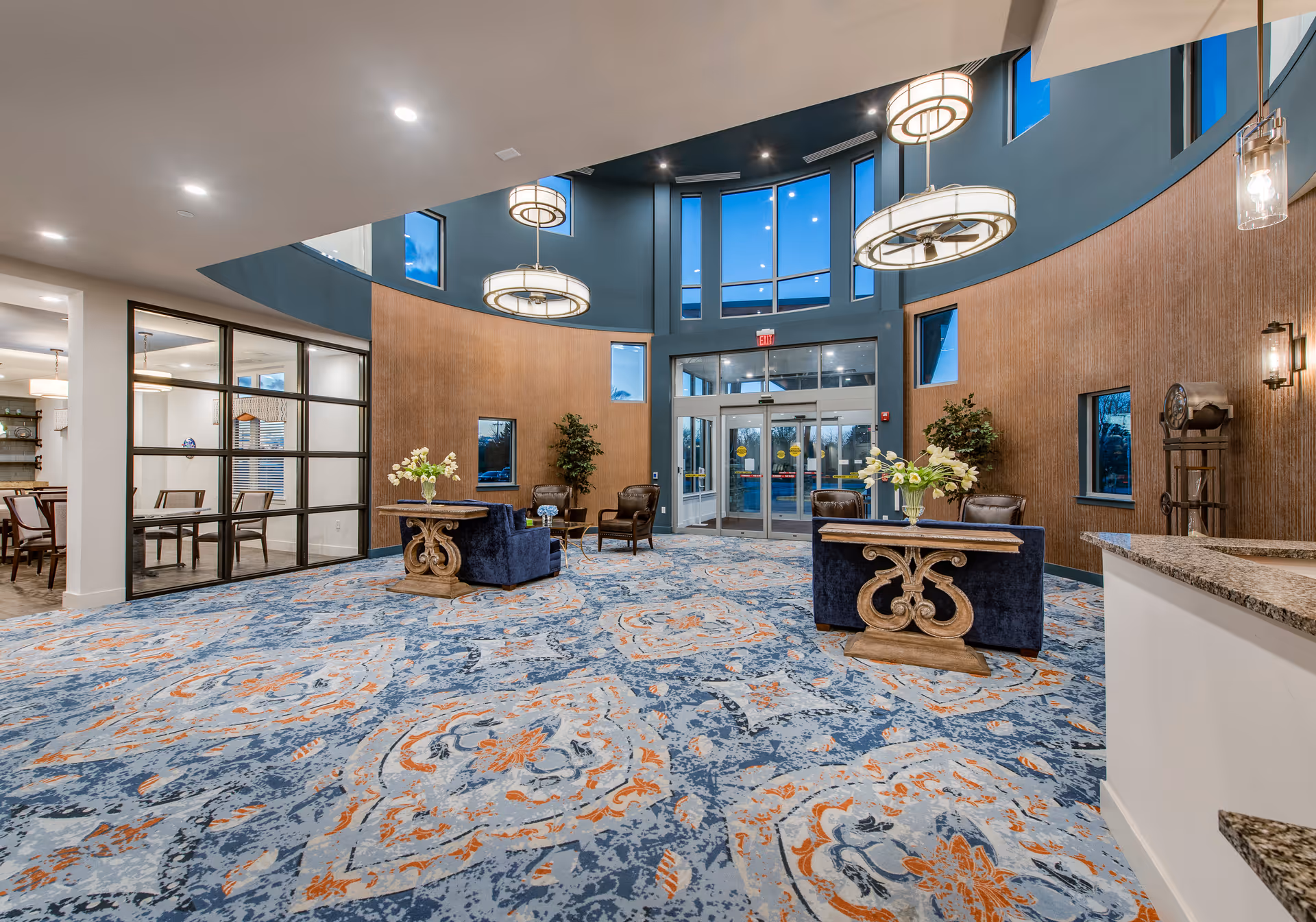 Spacious curved-entry lobby with patterned carpet, seating areas, decorative tables, and glass double entrance doors.