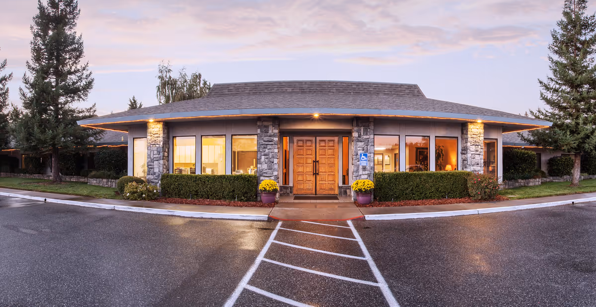 Exterior front view of Crystal Ridge Care Center building at dusk with illuminated entrance, stone pillars, large windows, and surrounding trees and landscaping.