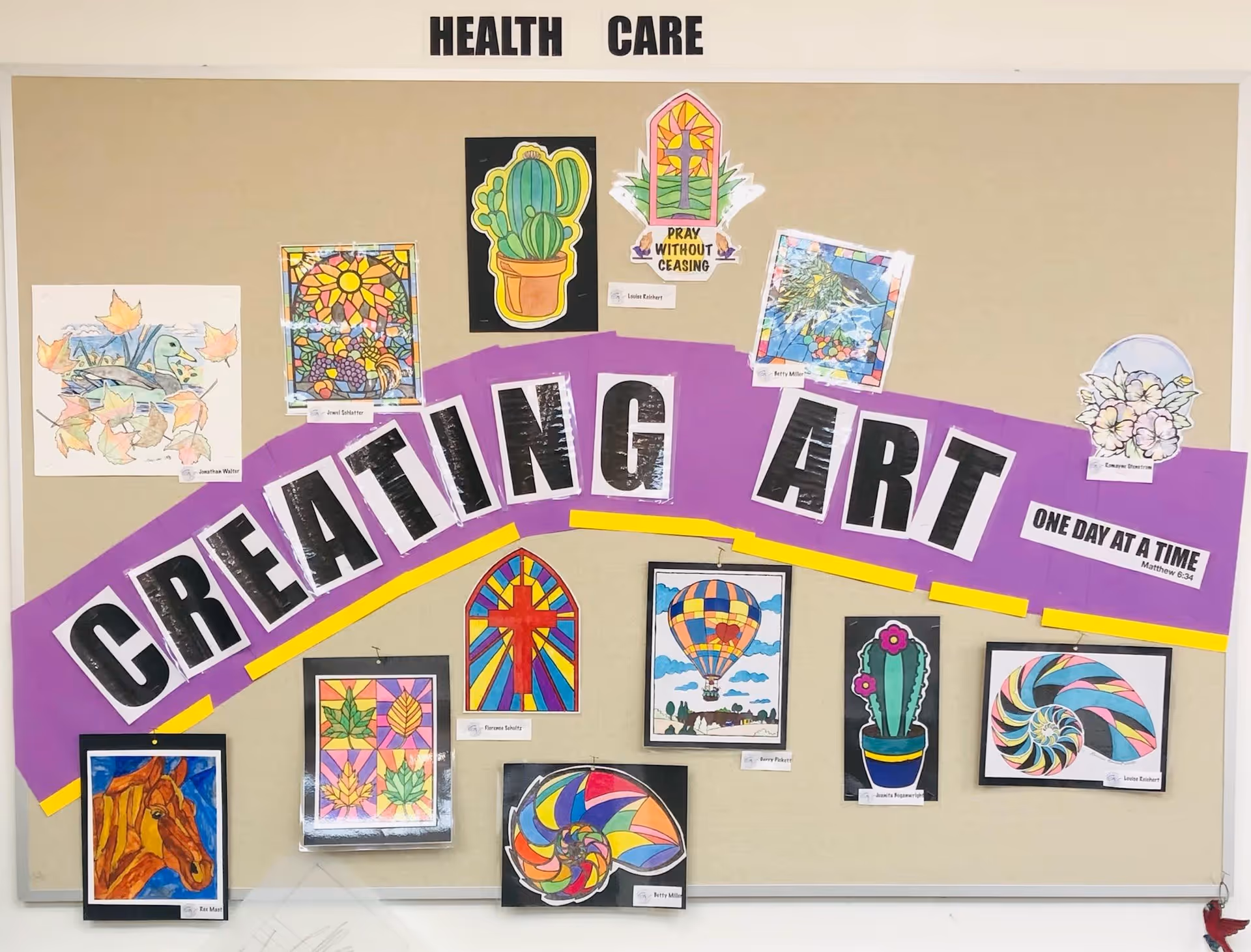 A bulletin board titled 'Creating Art' with various colorful artwork pieces displayed, including drawings of a horse, stained glass designs, cacti, flowers, and a hot air balloon. The board also features inspirational messages such as 'Pray Without Ceasing' and 'One Day At A Time.'