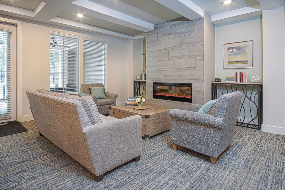 Cozy seating area with sofas and armchairs around a coffee table facing a wall-mounted electric fireplace in a lounge.