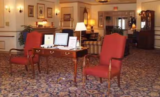 A well-lit senior living lobby featuring red upholstered chairs, a desk with pamphlets, and art.