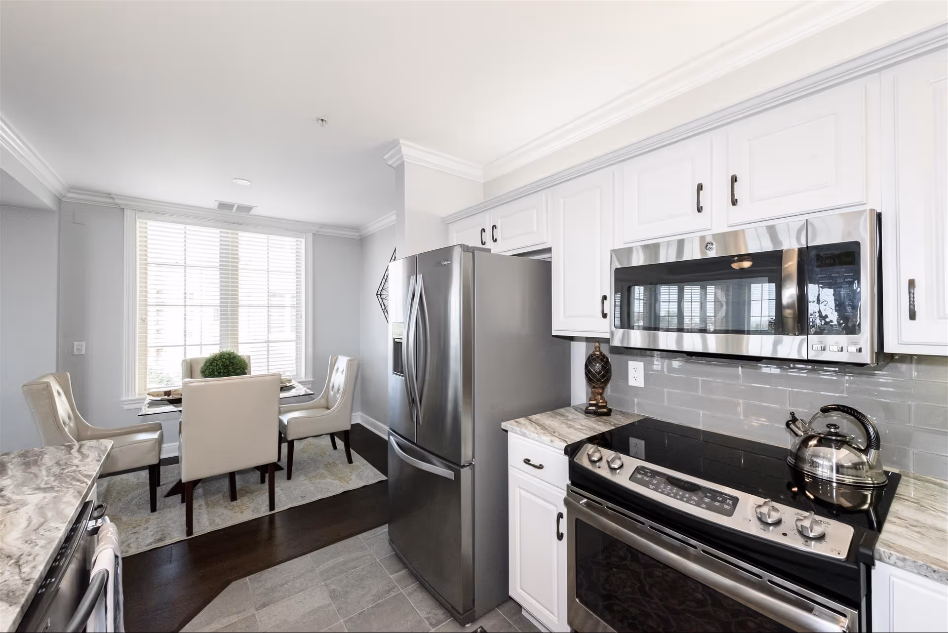 Bright modern kitchen with stainless steel appliances and a small dining table by a large window.