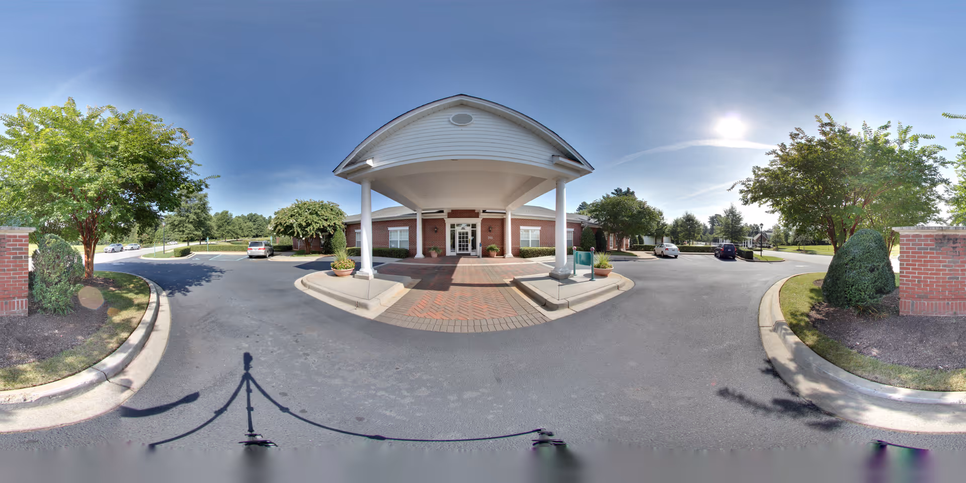 Front entrance of Oaks at Chanticleer showing a covered porte-cochere, circular driveway, parked cars, and landscaped trees and shrubs.