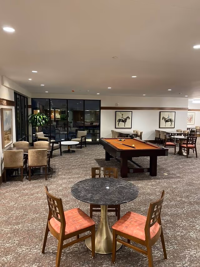 Spacious communal lounge with round tables and chairs, a pool table in the center, and artwork on the walls.