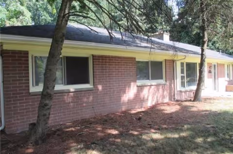 Exterior view of a single-story brick building with windows and shaded surroundings.