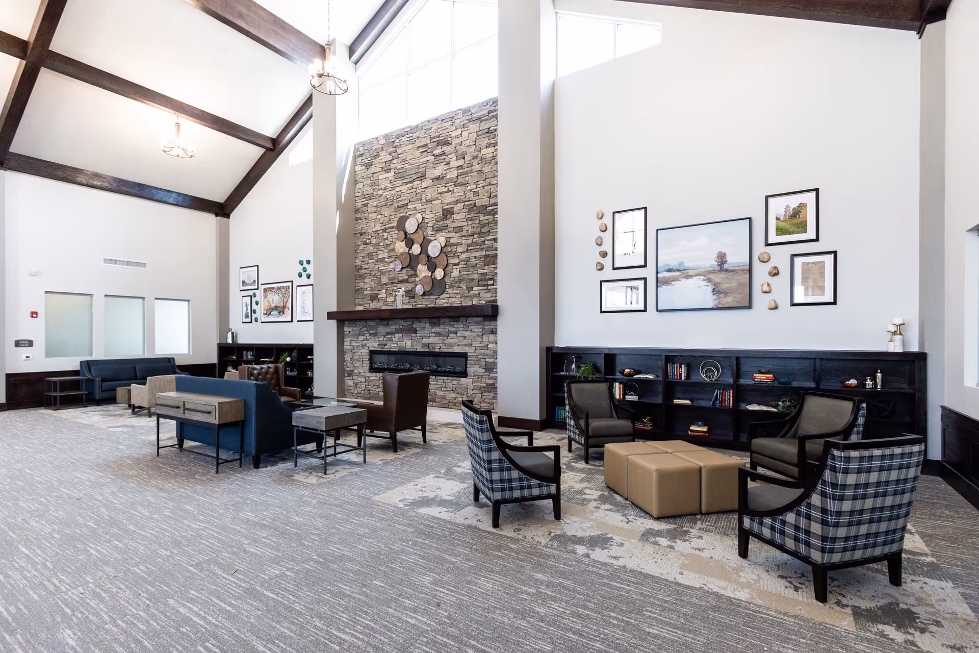 Spacious senior living lounge with vaulted ceilings, a stone fireplace, multiple seating areas, bookshelves and wall art.