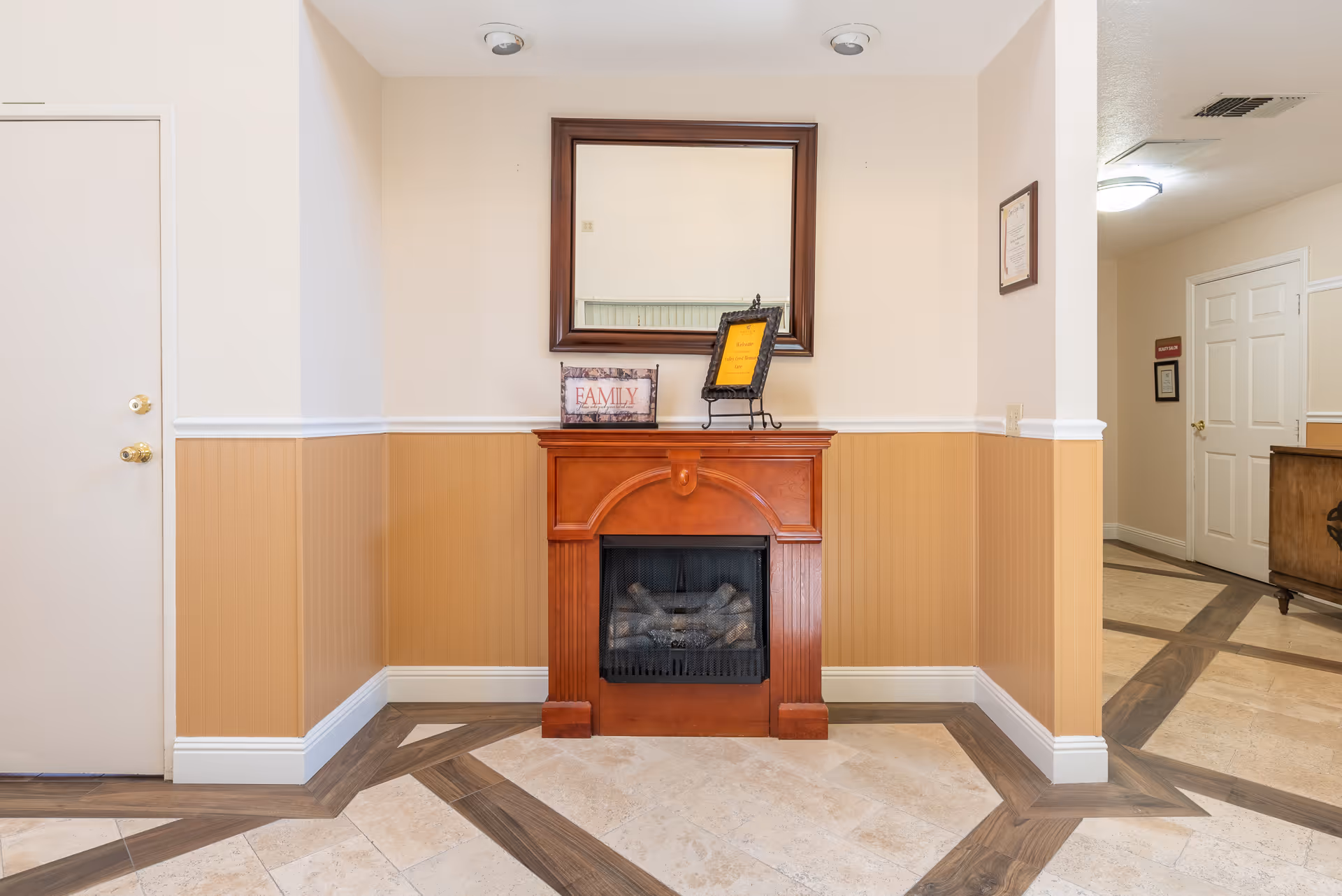 Decorative wooden fireplace with a mirror above and a 'Family' sign on the mantel in a clean hallway interior.