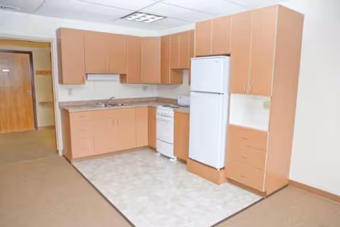 Compact kitchenette with brown cabinets, refrigerator, stove, and sink in an interior room.