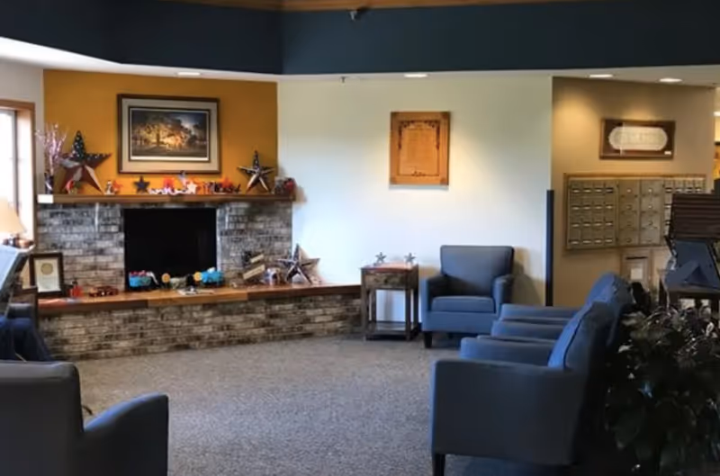 Common room with blue armchairs, a brick fireplace decorated with star ornaments and a painting, and mailboxes on the right.