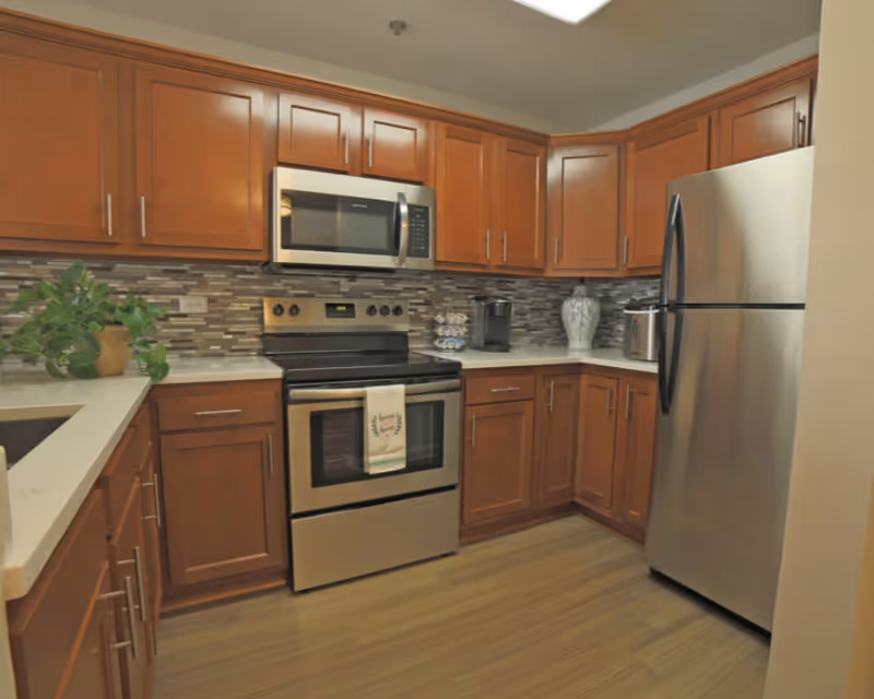A U-shaped kitchen with wooden cabinets, stainless steel refrigerator, oven and microwave, and a mosaic tile backsplash.