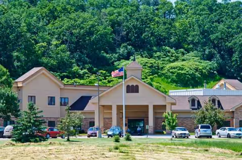 Front view of a beige senior living center with parked cars and an American flag.