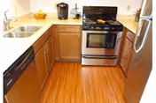 U-shaped kitchen with stainless steel stove and refrigerator, wooden cabinets, white countertops, sink, dishwasher, and hardwood floors.