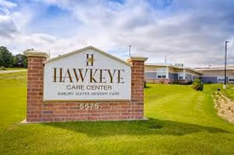 A brick sign reading Hawkeye Care Center sits on a grassy lawn with a building behind.
