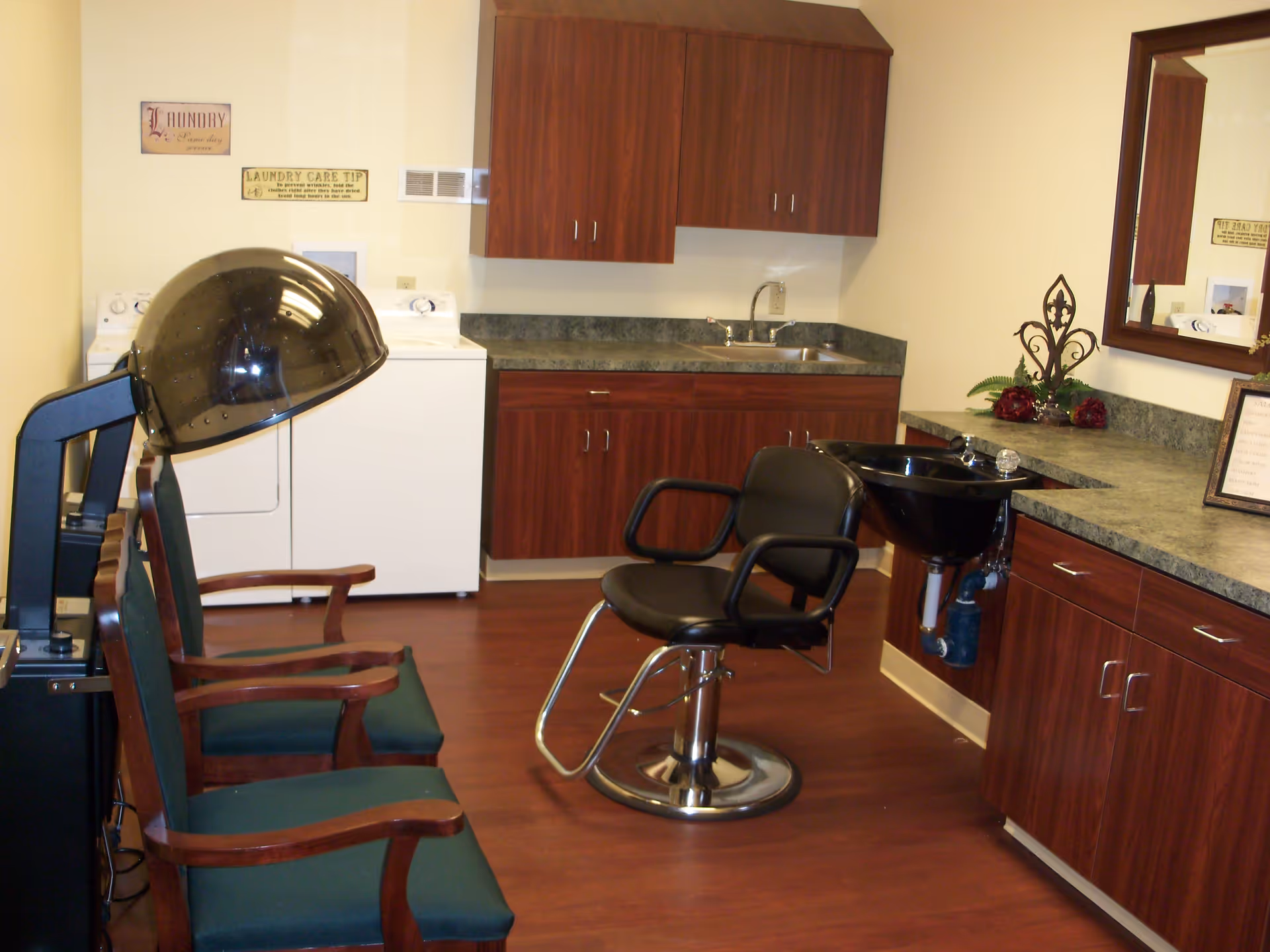 A salon-style room with styling chairs, a hair-washing sink and hooded dryer, wood cabinets, and a washer and dryer.