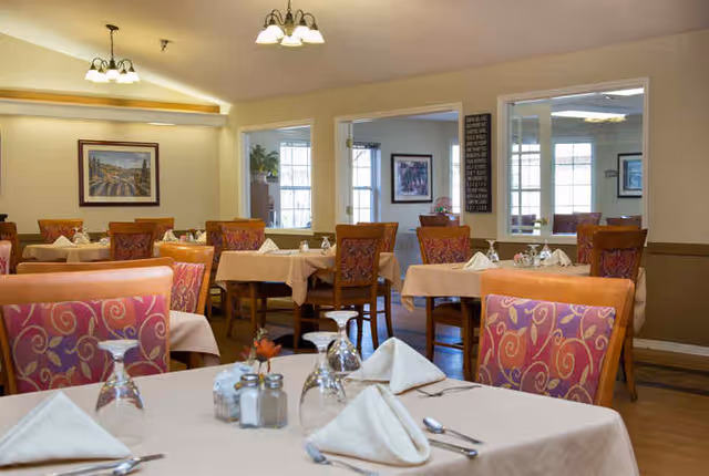 Well-lit dining room with tables set with napkins, glassware, and colorful upholstered chairs.