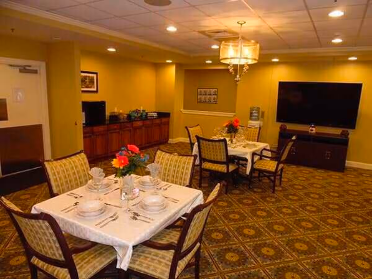 Small dining room with set tables and chairs, floral centerpieces, a wall-mounted TV and a buffet cabinet.