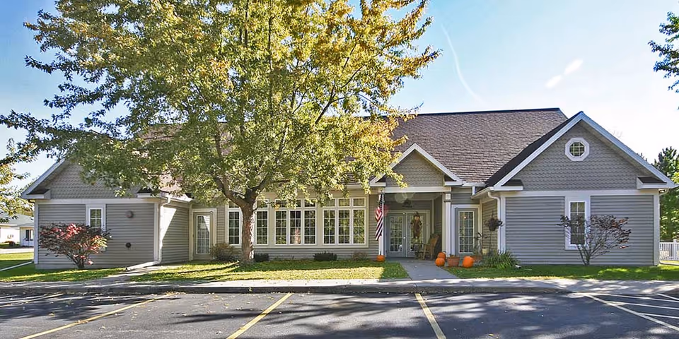 A single-story senior living facility with a front entrance, tree, and pumpkins.