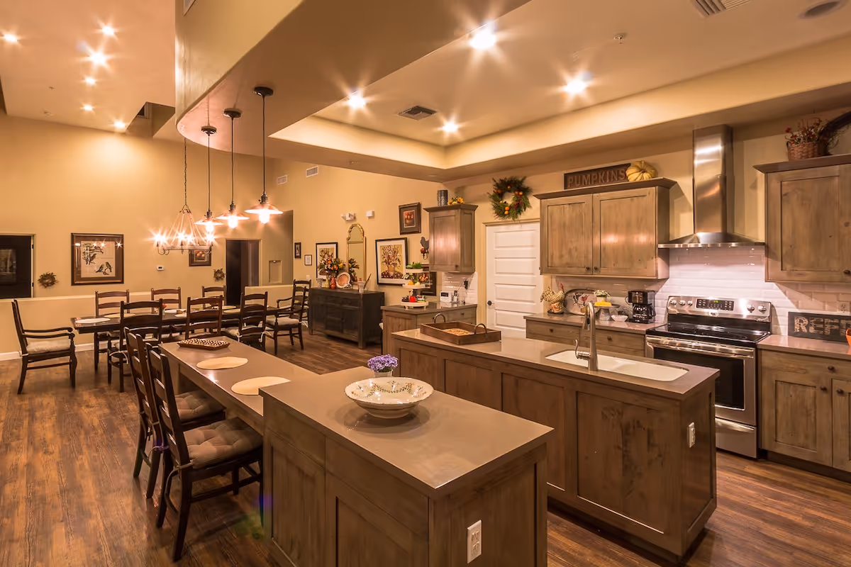 Open-plan kitchen and dining area with a large island, wooden cabinets, stainless steel appliances, and a long dining table.