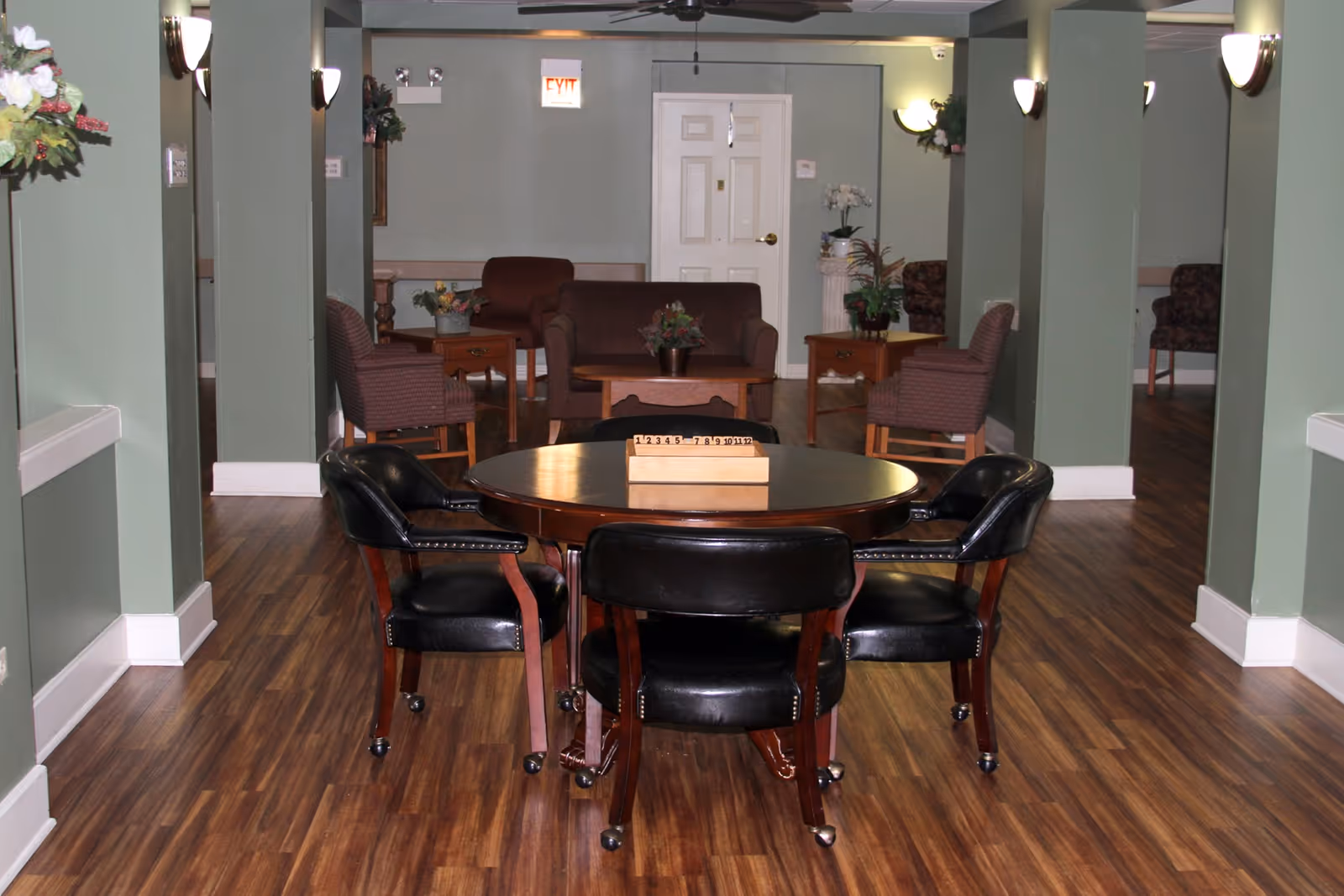 A senior living facility common room with a round table and four leather chairs in the foreground and sofas and armchairs in the background.