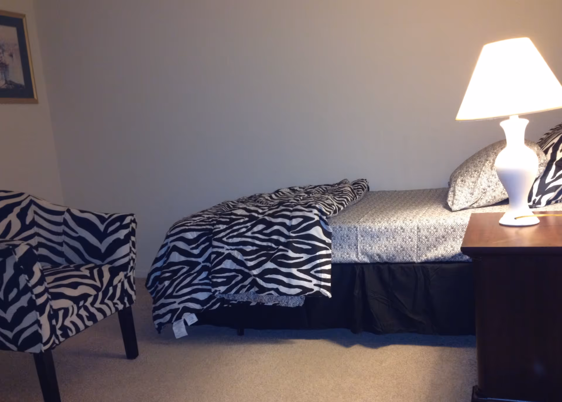 Small bedroom with a zebra-print bedspread and matching chair beside a nightstand with a lamp.