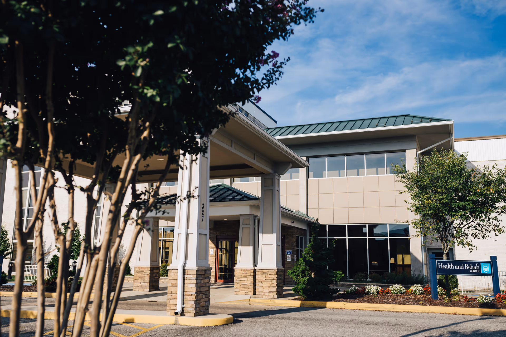 Exterior view of Friendship Health & Rehab Center North showing the entrance with a covered drop-off area, trees, and landscaping under a partly cloudy sky.
