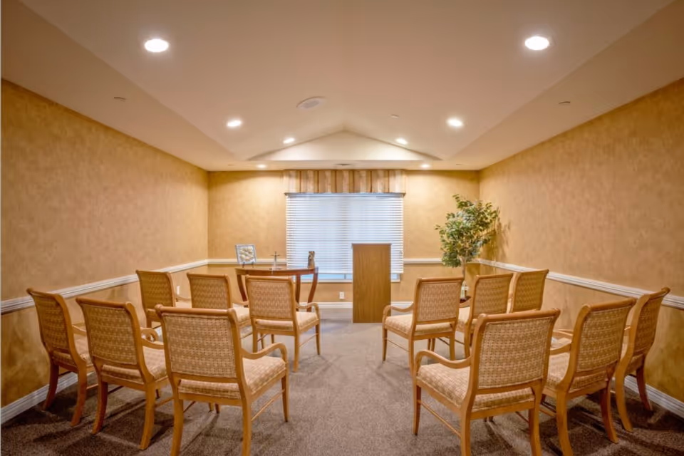 Small meeting room with rows of chairs facing a podium and table beneath recessed ceiling lights.