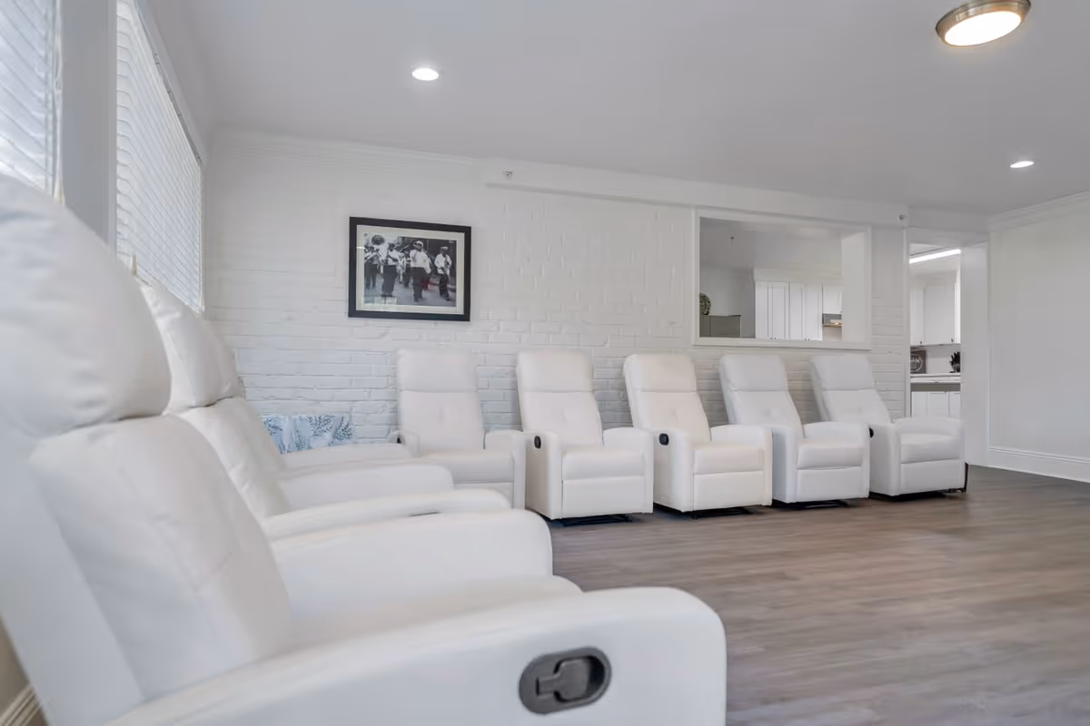 Bright common lounge with a row of white recliner chairs against a white brick wall.