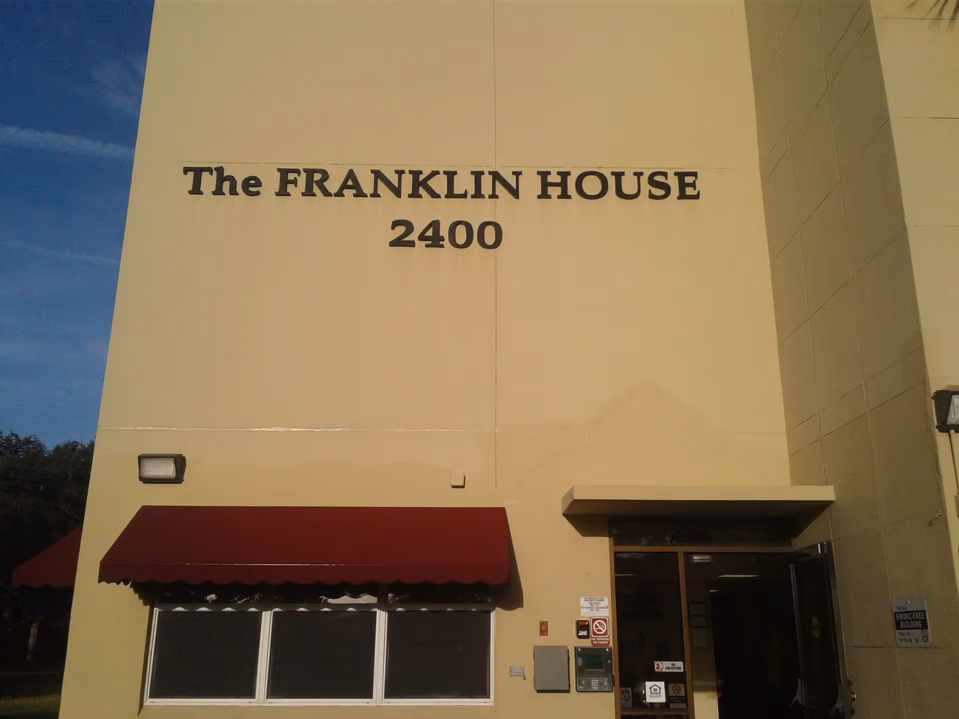 Exterior front facade of The FRANKLIN HOUSE with the number 2400 above an entrance and windows with a red awning.