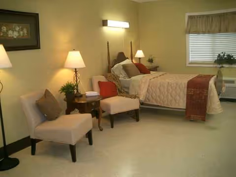 Cozy furnished bedroom in Vermillion Convalescent Center with bed, chairs, lamps, and window.