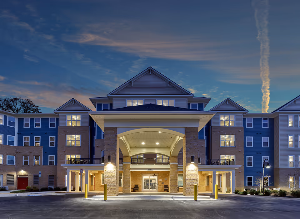 Front entrance of a modern senior living facility with a covered driveway at dusk.