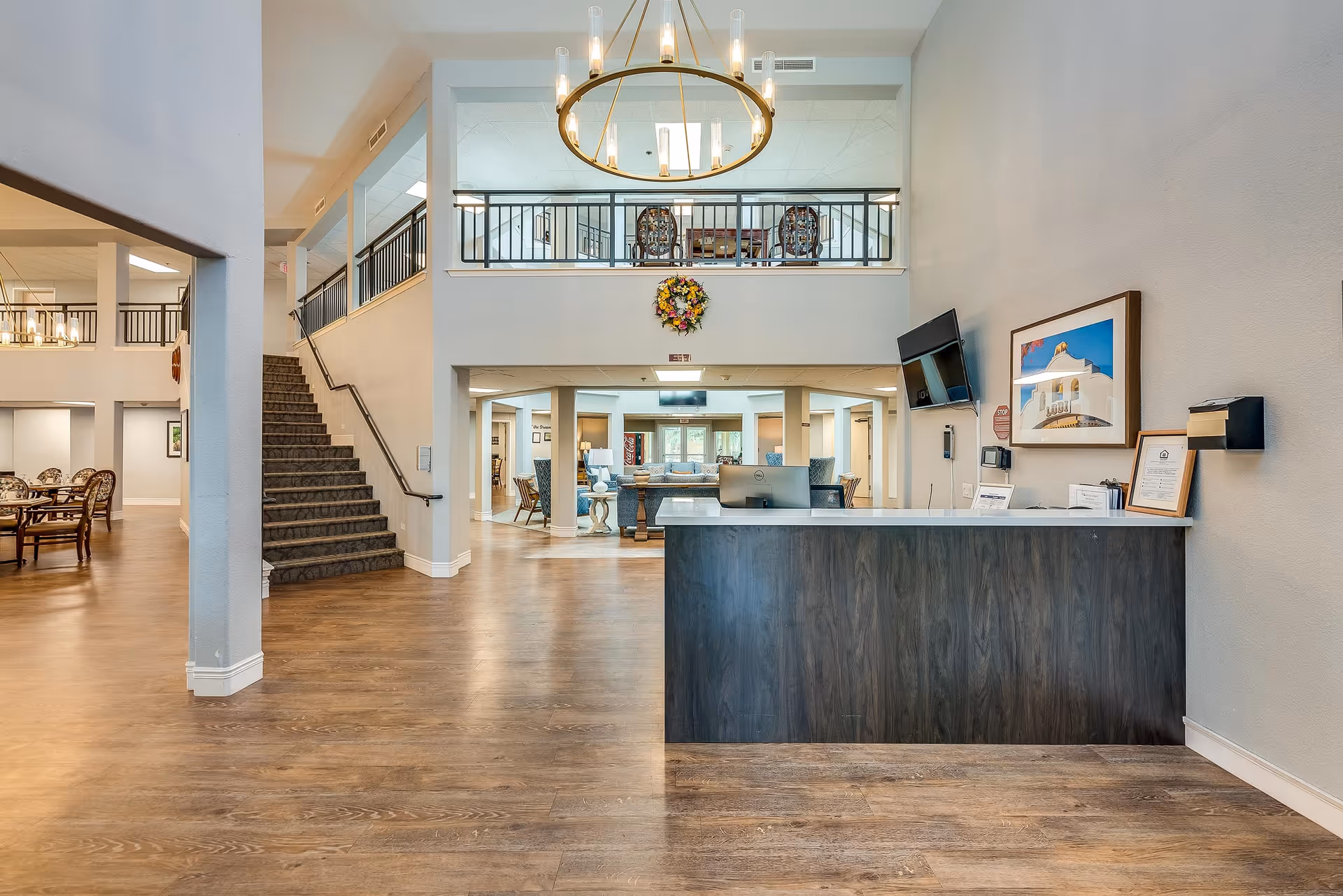Bright, spacious senior living lobby with a reception desk, staircase, seating area and chandelier.