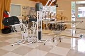 Physical therapy room with parallel bars, exercise equipment and wheelchairs in a tiled interior.