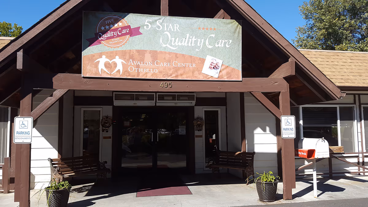 Front entrance of Avalon Care Center Othello showing a covered entry with benches, potted plants, a mailbox, and a '5-Star Quality Care' banner.