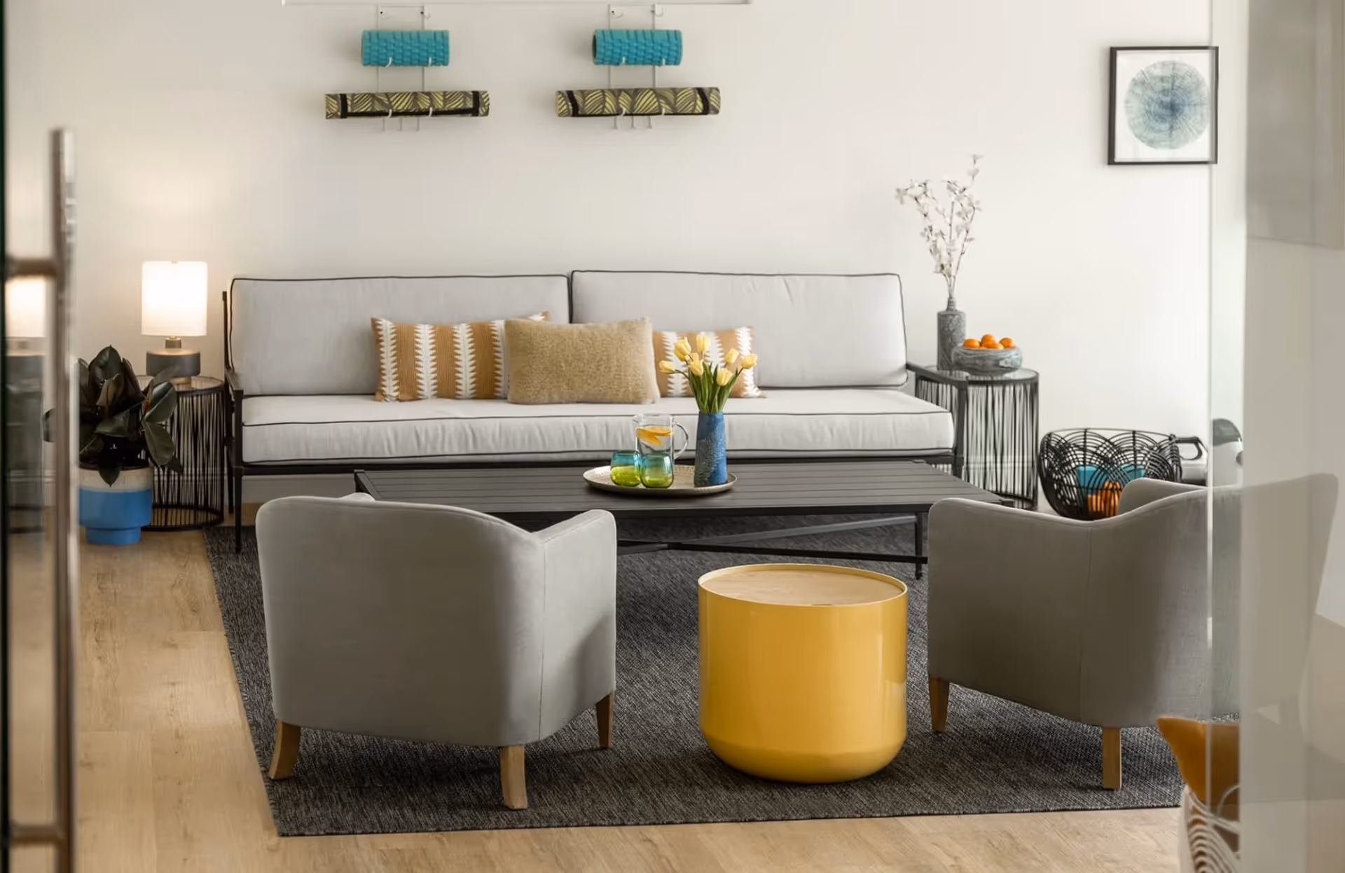 Modern living room with a white sofa, two gray armchairs, a yellow drum side table and a coffee table on a dark rug.