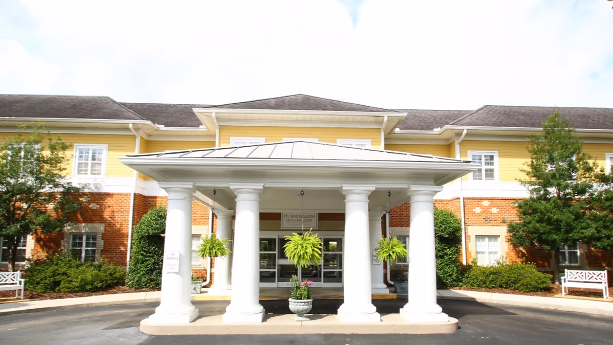 Front entrance of Morningside of Wilmington with a white-columned portico, hanging ferns, and a brick-and-yellow facade.