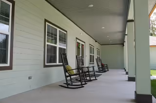 Covered exterior porch with several black rocking chairs lined up along the light green building.
