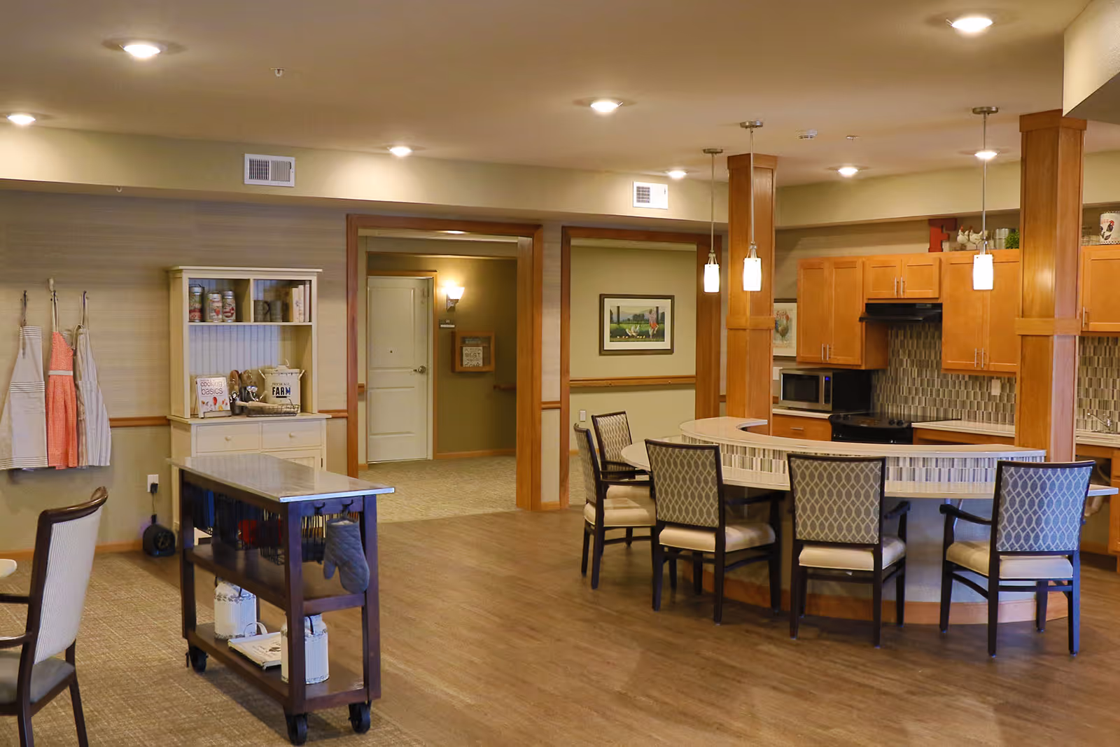 A senior living communal kitchen and dining area with a curved island, chairs, and cabinetry.