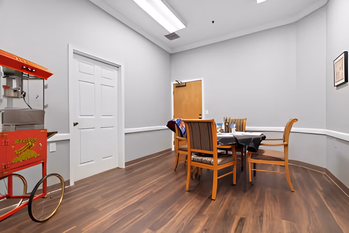 Small dining area with a table and chairs in a gray-walled room and a vintage popcorn cart against the wall.